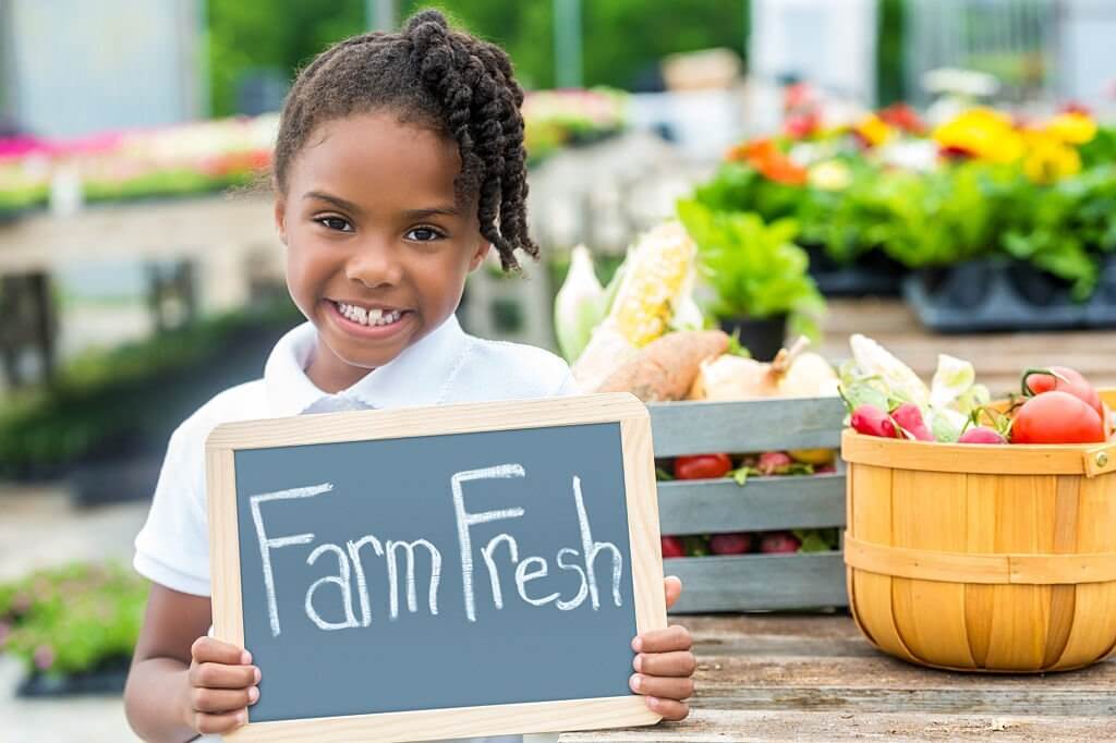 Young African American girl at farmers market with farm fresh sign.